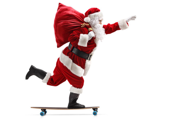 Full length profile shot of Santa Claus riding a longboard isolated on white background - Foto, immagini