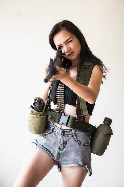 Asian sexy woman in soldier uniform aiming an assault M16 rifle gun with many bullets and vacuum bottle. Beautiul Female warrior or terrorist with copy space for text. - Foto, afbeelding