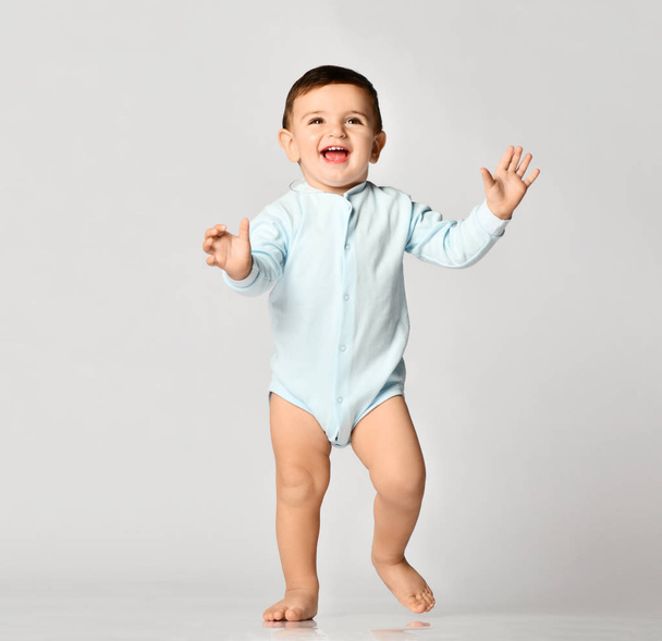 Infant child baby boy kid toddler in light blue body cloth make first steps on grey   - Foto, afbeelding
