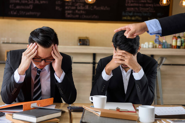 angry boss pointing his finger to working team to complaint for project delay and failure while both young businessmen raise hands to close or cover their faces. - 写真・画像