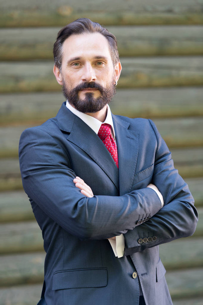 Waist up of attractive elegant man with dark hair and beard standing with his arms crossed and looking calm - Фото, изображение