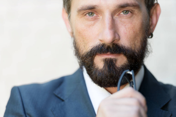 Thoughtful middle aged bearded man holding glasses near his chin and looking serious - Foto, Imagem