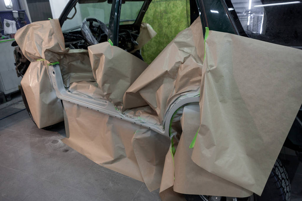 Schilderen deel van elementen van het lichaam van de groene auto in de werkplaats voor reparatie van het lichaam. SUV auto bedekt met papier van het raken van de verf. - Foto, afbeelding