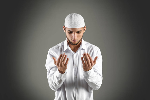 Young Muslim man praying on dark background - Фото, изображение
