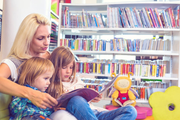A mãe com a menina e o menino leem o livro juntos. Família feliz, conceito pré-escolar. Filhos educativos dos pais
. - Foto, Imagem