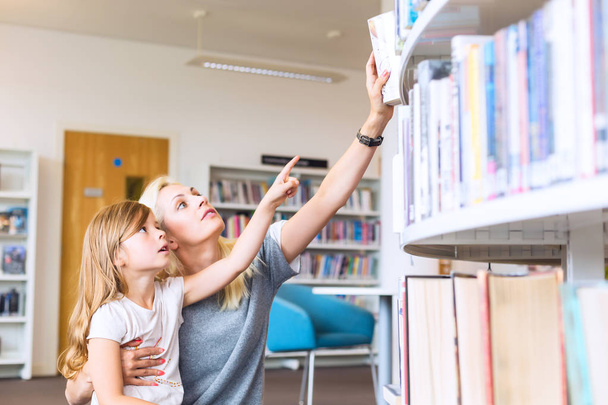 Mãe com filha escolhendo livro na biblioteca. Família feliz, pré-escola, conceito de educação
.  - Foto, Imagem