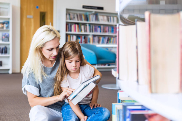 Anya lánya olvasható könyvvel együtt könyvtárában. Boldog családi, óvodai koncepciója. Szülő oktatási gyerekek. - Fotó, kép