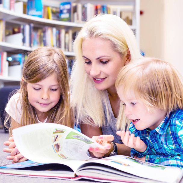 Äiti, jolla on pieni tyttö ja poika luki kirjaa yhdessä. Onnellinen perhe, esikoulu. Vanhempien kouluttaminen
. - Valokuva, kuva