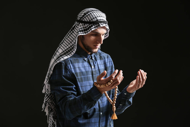 junger muslimischer Mann mit Rosenkranzperlen, die auf dunklem Hintergrund beten - Foto, Bild
