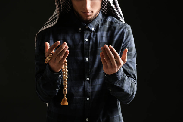 Young Muslim man with rosary beads praying on dark background - Фото, изображение