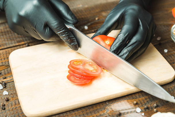 Γυναικεία χέρια κόβουμε τη ντομάτα, δίπλα στο ψέμα η πάπρικα, βότανα, αγγούρια και καρυκεύματα - Φωτογραφία, εικόνα