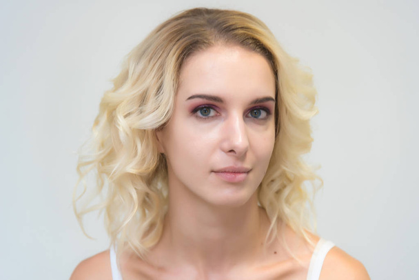 Beauty portrait of a beautiful blonde girl on a white background with perfect makeup. Beauty style model is right in front of the camera and looks happy. - Φωτογραφία, εικόνα
