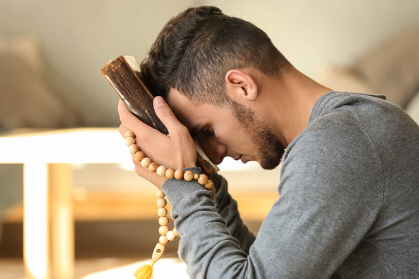 Young Muslim man with Koran praying at home - Photo, image