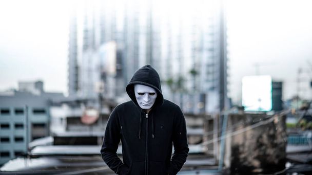 Mysterieuze hoodie man in een wit masker reputatie in de regen op het dak van een verlaten gebouw. De bipolaire wanorde of depressieve stoornis. Depressie concept - Foto, afbeelding