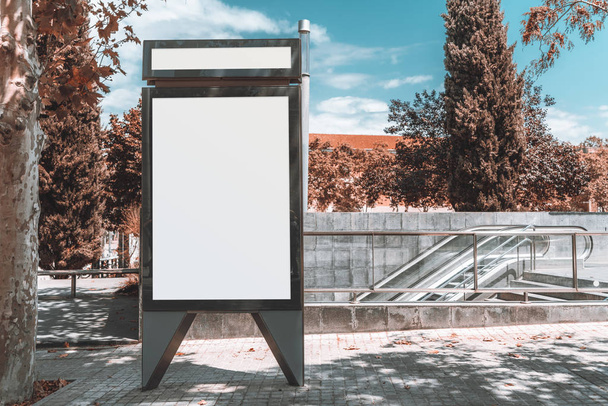 eine leere vertikale Platzhalter-Plakatwand-Vorlage auf der Straße mit U-Bahn-Eingang dahinter; leere Werbebanner-Attrappe im Park einer europäischen Stadt, U-Bahnübergang im Hintergrund - Foto, Bild