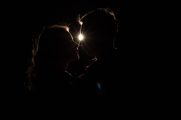 black background, silhouette of couples, heads, between them a light, a ray of light unfinished kiss.the beginning of a kiss. - Фото, зображення