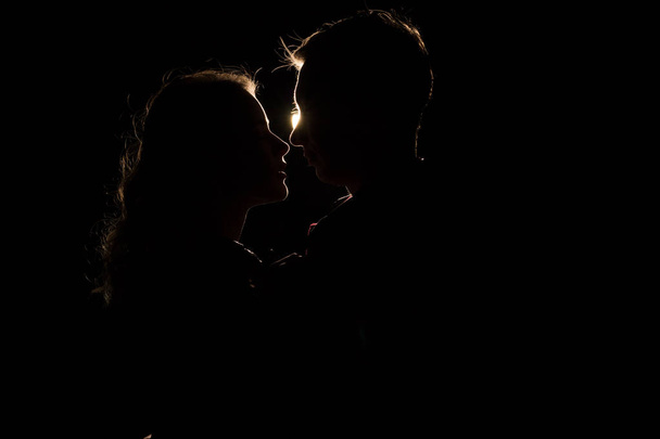 fond noir, silhouette de couples, têtes, entre eux une lumière, un rayon de lumière baiser inachevé.le début d'un baiser
. - Photo, image