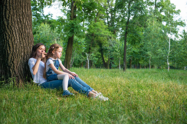 Mom and daughter are sitting near a tree - Photo, Image