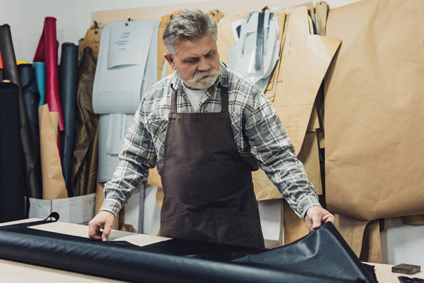 mature tailor in apron working with leather at workshop - Photo, Image