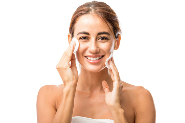 Портрет счастливой женщины, снимающей макияж с хлопчатобумажными прокладками в студии
 - Фото, изображение