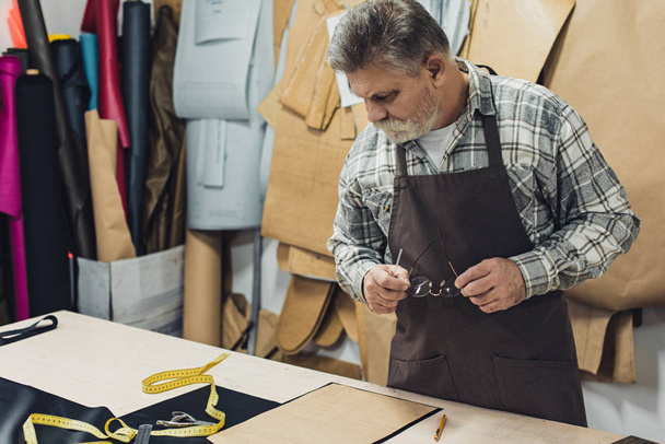 artesano bolso de cuero masculino en delantal trabajando en el estudio
 - Foto, imagen