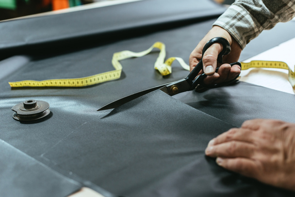 cropped image of male handbag craftsman cutting leather by scissors at workshop - Photo, Image
