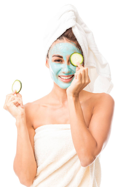 Gorgeous woman smiling while holding cucumber slices undergoing beauty treatment on white background - Fotó, kép