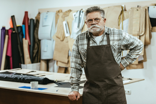Selbstbewusster Handwerker in Schürze und Brille posiert im Atelier - Foto, Bild