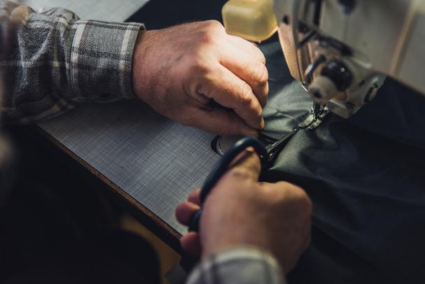cropped image of male handbag craftsman cutting leather near sewing machine at studio - Foto, Imagem