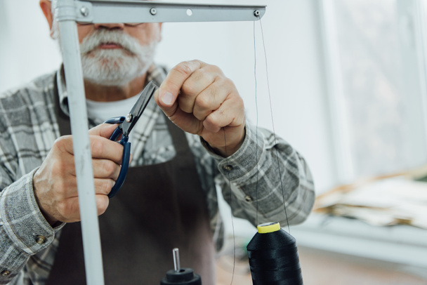image recadrée du tailleur d'âge moyen dans les cordes de coupe de tablier sur la machine à coudre à l'atelier
 - Photo, image