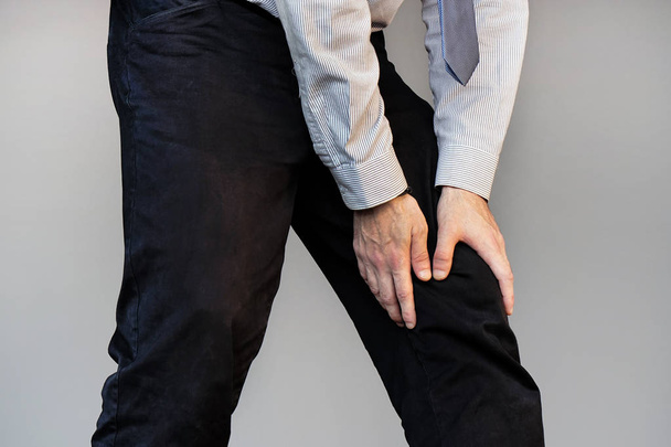 Pijn In de knie. Close-up zakenman been met pijnlijke Kneeson geïsoleerd op een grijze achtergrond. Man het gevoel van pijn in de gewrichten, problemen van gezondheid en been met de handen aan te raken. Lichaam en Health Care Concept. - Foto, afbeelding