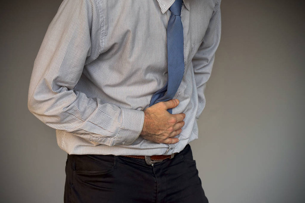 Hombre sosteniendo su estómago con dolor aislado sobre fondo gris. Empresario que sufre de dolor abdominal. Concepto de Cuerpo y Cuidado de la Salud
. - Foto, Imagen