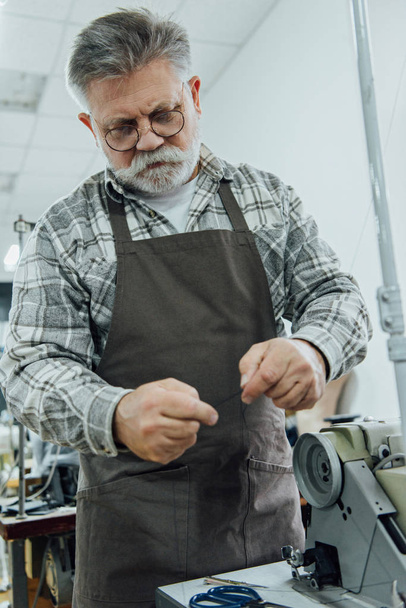 низький кут зору чоловіка середнього віку, який працює біля швейної машини в студії
 - Фото, зображення