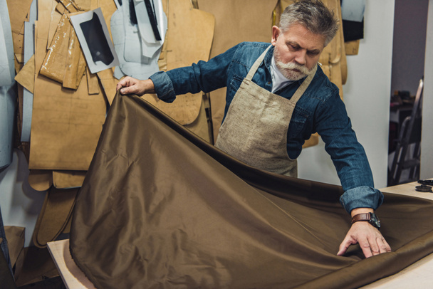middle aged male handbag craftsman putting fabric on working table at studio - Photo, Image