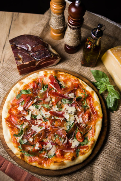 hot fresh pizza wit cheese,ham and basil on wooden plate - Photo, image
