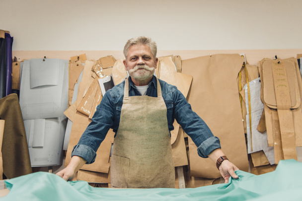allegro maturo uomo borsetta artigiano mettendo tessuto sul tavolo di lavoro in studio
 - Foto, immagini