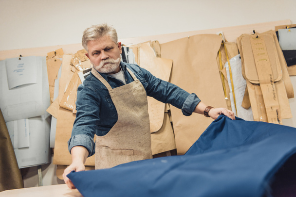 sério meia idade masculino bolsa artesão colocando tecido na mesa de trabalho no estúdio
 - Foto, Imagem