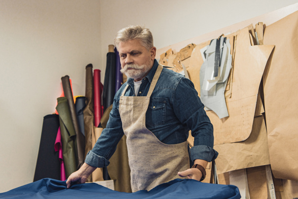 confident male handbag craftsman putting fabric on working table at studio - Photo, Image