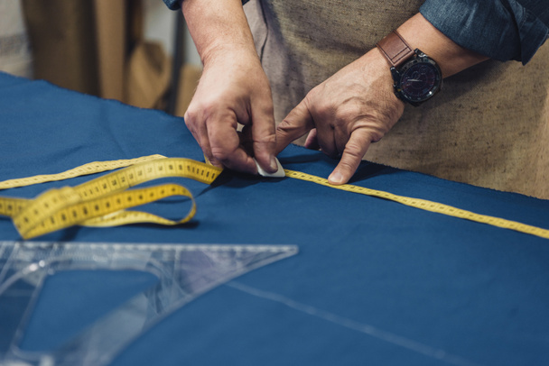 cropped image of male craftsman in apron making measurements on fabric at workshop - 写真・画像