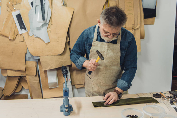 artesano de bolso masculino de mediana edad enfocado que trabaja con martillo en el estudio
 - Foto, Imagen