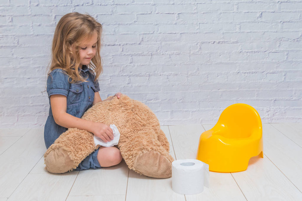 a against the background of a white brick wall, the girl sits on a potty with the child, wiping her ass with toilet paper - Фото, изображение
