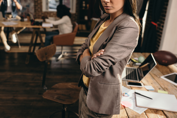 обрезанный вид деловой женщины, стоящей за столом в лофт-офисе с коллегами на заднем плане
 - Фото, изображение