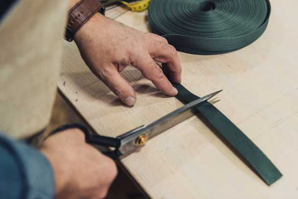 cropped image of male handbag craftsman cutting fabric by scissors at workshop - Photo, Image