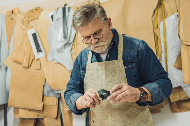 中間の老化させた男性ハンドバッグ職人エプロン、眼鏡工房布で作業を集中してください。 - 写真・画像
