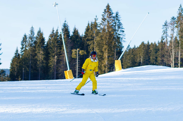 Woman in yellow winter jumpsuit riding skis in snowy mountains  - Photo, Image