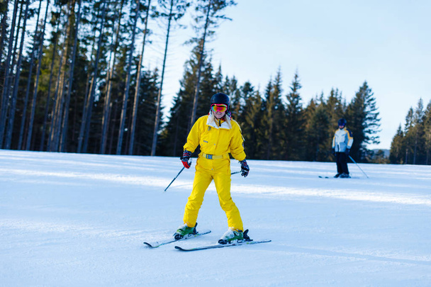 Жінка в жовтому зимовому комбінезоні катається на лижах у засніжених горах
  - Фото, зображення