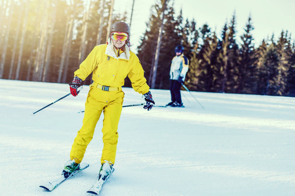 Woman in yellow winter jumpsuit riding skis in snowy mountains  - Photo, Image