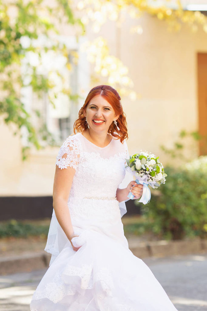 Beautiful redhead bride with bouquet outdoor. Happy bride jumping and having fun outdoors. Beautiful bride posing in her wedding day - Foto, Bild