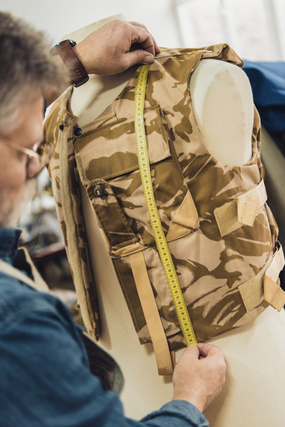 vista parcial del sastre macho maduro haciendo mediciones en chaleco militar en el taller
 - Foto, imagen