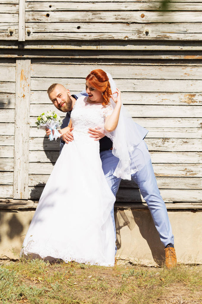 Just married loving hipster couple in wedding dress and suit posing in front of an old wooden house. Happy bride and groom walking running and dancing. Romantic Married young family. Autumn wedding - Photo, Image